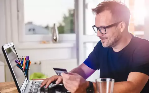 Person smiling at computer with credit card in hand