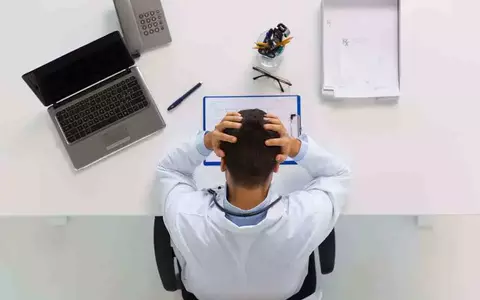 Person holding their head in their hands looking at paper on desk