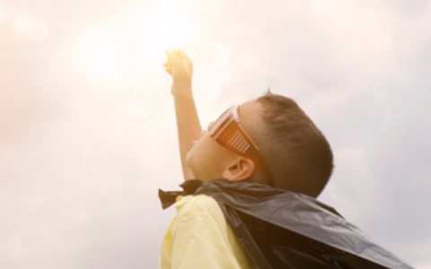 Young boy with cape and glasses pretending to fly