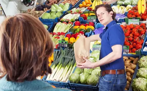 Green Grocer Serving A Customer Filling A Brown Paper Bag With Peppers