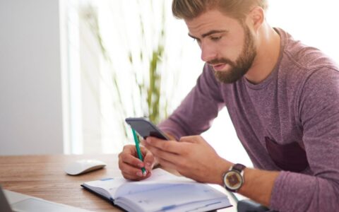 Person looking at his phone making notes in diary