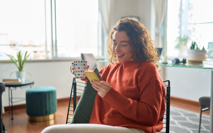 Young smiling pretty woman holding smartphone technology drinking tea